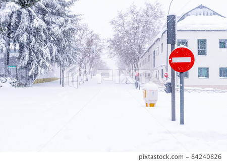 View of a city street covered in snow during heavy snowfall with fallen trees View of a city street covered in snow during heavy snowfall with fallen trees 84240826