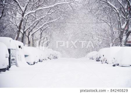 View of city street covered in snow during heavy snowfall with trapped vehicles View of city street covered in snow during heavy snowfall with trapped vehicles 84240829