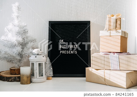 Many craft Christmas gift boxes and black letter board with quote Ok but first presents. Festive Christmas letter board ideas and quotes. Blackboard with the Xmas phrase on table Many craft Christmas gift boxes and black letter board with quote Ok but first presents. Festive Christmas letter board ideas and quotes. Blackboard with the Xmas phrase on table 84241165