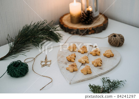 Cozy Christmas mood. Craft homemade cookies Christmas tree shape in wooden tray on table with fir tree branch and candles Cozy Christmas mood. Craft homemade cookies Christmas tree shape in wooden tray on table with fir tree branch and candles 84241297