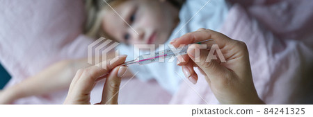 Woman hand holding mercury thermometer with high temperature against background of sick girl closeup 84241325