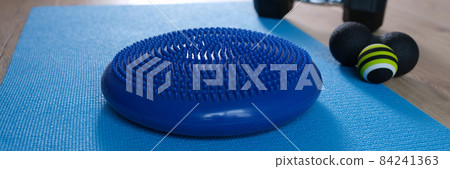 Blue balance cushion lying on mat near dumbbells and roll ball home closeup 84241363