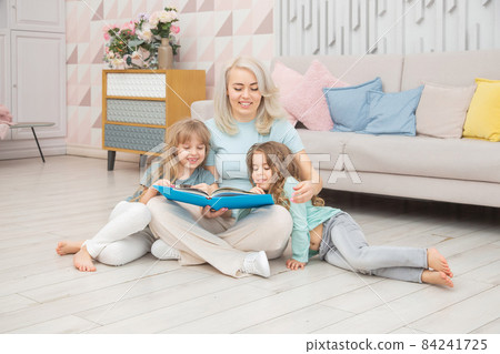Smiling caucasian mom teaching daughters sitting on the floor Smiling caucasian mom teaching daughters sitting on the floor 84241725