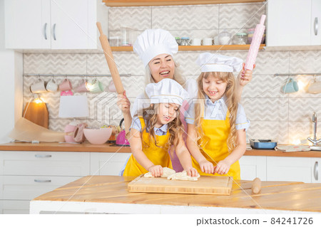 Happy caucasian mother helping her preschool daughters rolling dough Happy caucasian mother helping her preschool daughters rolling dough 84241726