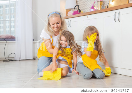 Smiling caucasian mom teaching daughters wet cleaning the kitchen. Smiling caucasian mom teaching daughters wet cleaning the kitchen. 84241727