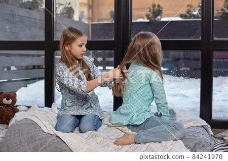 The image of two cute little sisters sitting on windowsill in peace and quiet 84241970