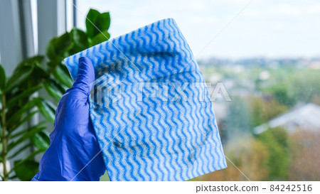 Employee hand in rubber protective glove holding dirty micro fiber cloth wiping window from dust. General spring cleaning. Housework and housekeeping concept Employee hand in rubber protective glove holding dirty micro fiber cloth wiping window from dust. General spring cleaning. Housework and housekeeping concept 84242516