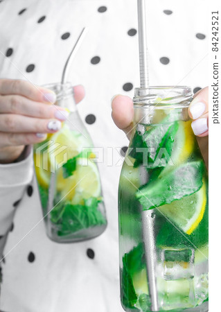 Female hand holding Mojito refreshing cocktail with eco metal drinking straw, alcohol drink. Lemonade with lemon and mint leaves. Summer refreshing detox drinks. Clean eating, healthy lifestyle 84242521