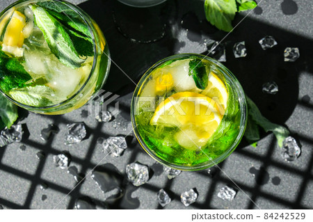 Mojito refreshing cocktail, alcohol drink. Lemonade with lemon and mint leaves on dark background. Trendy shadows Ice cubes. Summer refreshing detox drinks. Clean eating, healthy lifestyle concept. 84242529