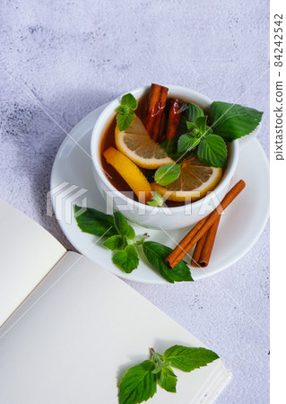 Black and green tea with lemon, cinnamon sticks and mint leaves on table with empty paper notebook. Personal diary Hot drink. Healthy melissa tea natural organic aromatic drink in cup. Summer, Autumn Black and green tea with lemon, cinnamon sticks and mint leaves on table with empty paper notebook. Personal diary Hot drink. Healthy melissa tea natural organic aromatic drink in cup. Summer, Autumn 84242542