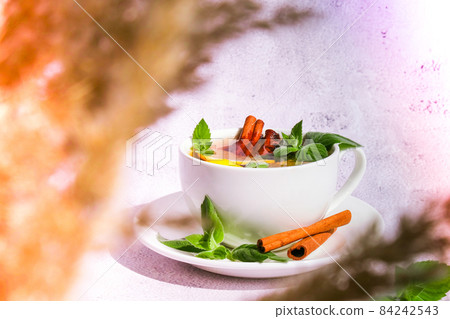 Black and green tea with lemon, cinnamon sticks and mint leaves. Hot drink. Healthy melissa tea natural organic aromatic drink in cup. Summer, Autumn winter warming drink. 84242543