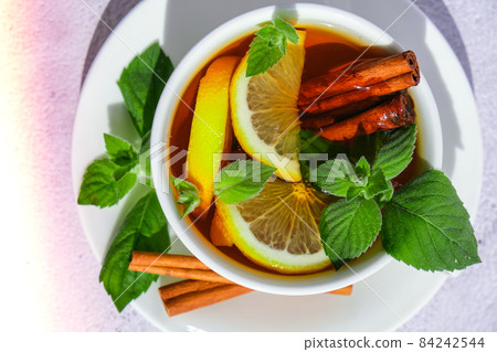Black and green tea with lemon, cinnamon sticks and mint leaves. Hot drink. Healthy melissa tea natural organic aromatic drink in cup. Summer, Autumn winter warming drink. 84242544