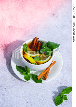 Black and green tea with lemon, cinnamon sticks and mint leaves. Hot drink. Healthy melissa tea natural organic aromatic drink in cup. Summer, Autumn winter warming drink. Black and green tea with lemon, cinnamon sticks and mint leaves. Hot drink. Healthy melissa tea natural organic aromatic drink in cup. Summer, Autumn winter warming drink. 84242545