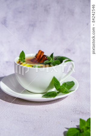 Black and green tea with lemon, cinnamon sticks and mint leaves. Hot drink. Healthy melissa tea natural organic aromatic drink in cup. Summer, Autumn winter warming drink. Black and green tea with lemon, cinnamon sticks and mint leaves. Hot drink. Healthy melissa tea natural organic aromatic drink in cup. Summer, Autumn winter warming drink. 84242546