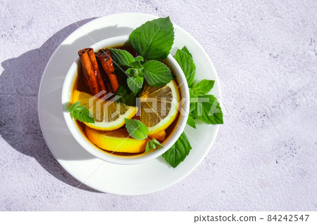 Black and green tea with lemon, cinnamon sticks and mint leaves. Hot drink. Healthy melissa tea natural organic aromatic drink in cup. Summer, Autumn winter warming drink. Black and green tea with lemon, cinnamon sticks and mint leaves. Hot drink. Healthy melissa tea natural organic aromatic drink in cup. Summer, Autumn winter warming drink. 84242547