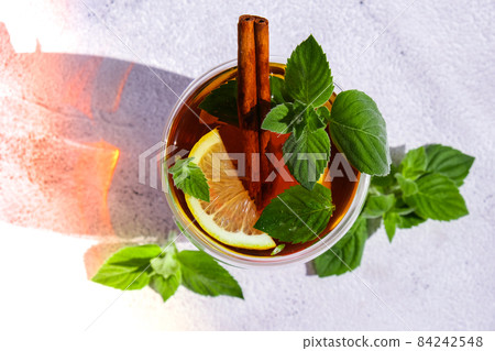 Black and green tea with lemon, cinnamon sticks and mint leaves. Hot drink. Healthy melissa tea natural organic aromatic drink in cup. Summer, Autumn winter warming drink. Black and green tea with lemon, cinnamon sticks and mint leaves. Hot drink. Healthy melissa tea natural organic aromatic drink in cup. Summer, Autumn winter warming drink. 84242548