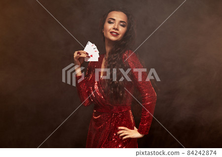 Young beautiful lucky brunette in a red evening dress shows her cards, a four of aces Young beautiful lucky brunette in a red evening dress shows her cards, a four of aces 84242874