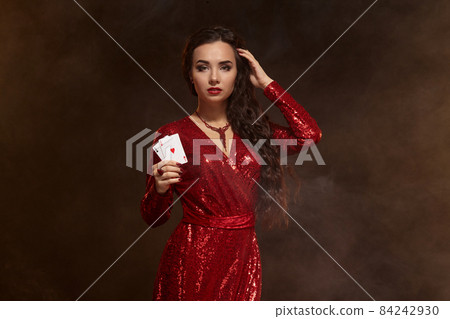Young beautiful lucky brunette in a red evening dress shows her cards, a pair of aces Young beautiful lucky brunette in a red evening dress shows her cards, a pair of aces 84242930