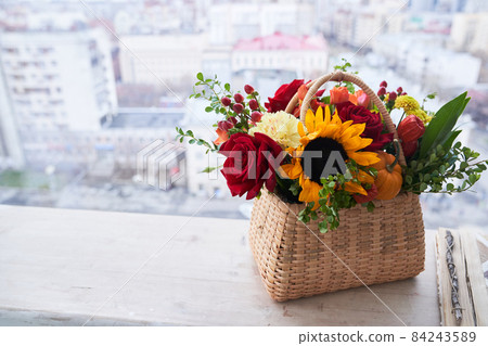 A basket with beautiful autumn flowers made of red roses, sunflowers and green leaves. The concept of the holiday. Copy space. High quality photo A basket with beautiful autumn flowers made of red roses, sunflowers and green leaves. The concept of the holiday. Copy space. High quality photo 84243589