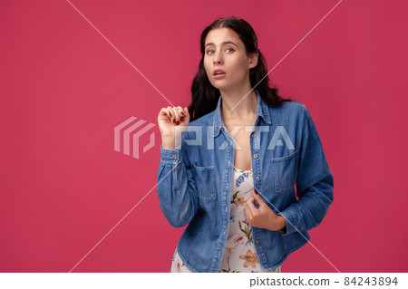 Portrait of a pretty young woman in a light dress and blue shirt standing on pink background in studio. People sincere emotions. 84243894