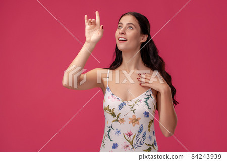 Portrait of a pretty young woman in a light dress standing on pink background in studio. People sincere emotions. 84243939