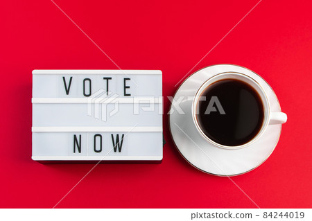 Vote now. Sign and cup of coffee on a red background. Election voting concept. Vote now. Sign and cup of coffee on a red background. Election voting concept. 84244019