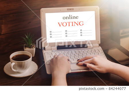 Woman votes online using laptop. Voting and elections concept. Work space at home. Woman votes online using laptop. Voting and elections concept. Work space at home. 84244077