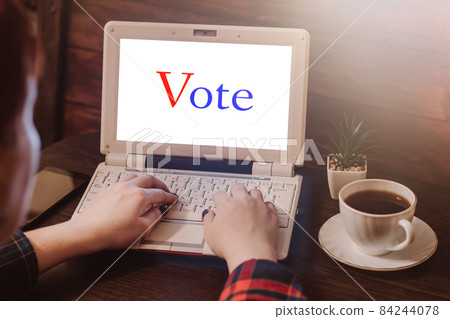 Woman votes online using laptop. Voting and elections concept. Work space at home. Woman votes online using laptop. Voting and elections concept. Work space at home. 84244078