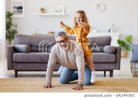 Cute little girl granddaughter playing and having fun with active positive grandfather at home Cute little girl granddaughter playing and having fun with active positive grandfather at home 84244365