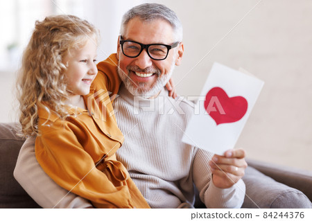 Cute little girl granddaughter giving handmade greeting card to smiling grandfather on Birthday Cute little girl granddaughter giving handmade greeting card to smiling grandfather on Birthday 84244376