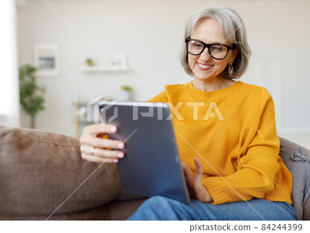 Portrait of happy smiling senior woman resting relaxing on sofa with tablet at home 84244399