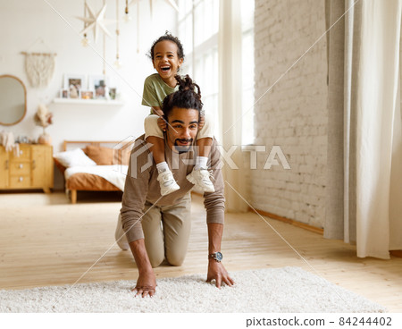 Young african american father giving piggyback ride to little son during playtime at home Young african american father giving piggyback ride to little son during playtime at home 84244402