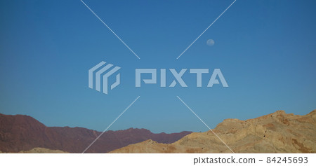 solitary moon at dusk, orange mountains and blue sky. desert landscape solitary moon at dusk, orange mountains and blue sky. desert landscape 84245693