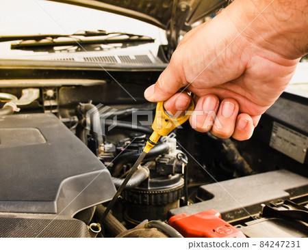 Mechanic hand pulling up oil dipstick of the car engine for checking oil level Mechanic hand pulling up oil dipstick of the car engine for checking oil level 84247231