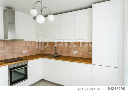 Modern kitchen interior with furniture and electrical appliances. Trendy stylish kitchen in white, beige-rose and wooden clear tones.  84248398