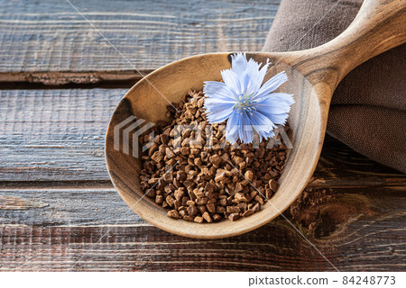Instant granules and flower of chicory in large wooden spoon 84248773