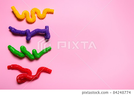 Colorful antistress pop tube toys on pink paper with large copy space 84248774