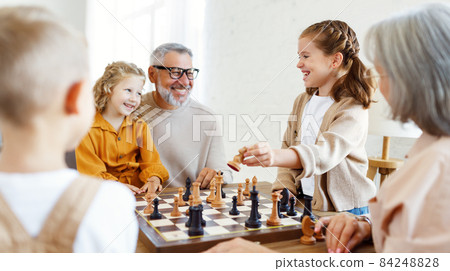 Children brother and sister playing chess while sitting in living room with senior grandparents 84248828