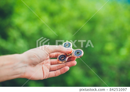 Close up of a man's hand who is holding a fidget spinner in a park 84251097