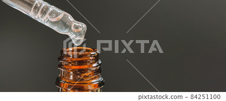 Pipette with a drop of face serum or oil for the face and hyaluronic acid on beautiful black background, close-up. Pipette with a drop of face serum or oil for the face and hyaluronic acid on beautiful black background, close-up. 84251100