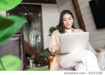 Young asian girl watching webinar on laptop. Girl relaxing with computer in hands at home, sitting on chair resting 84251596