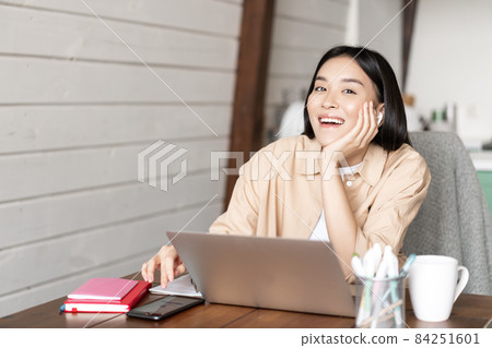 Happy asian girl listening online webinar, attend internet course classes on laptop, wearing wireless earphones and smiling, working from home Happy asian girl listening online webinar, attend internet course classes on laptop, wearing wireless earphones and smiling, working from home 84251601
