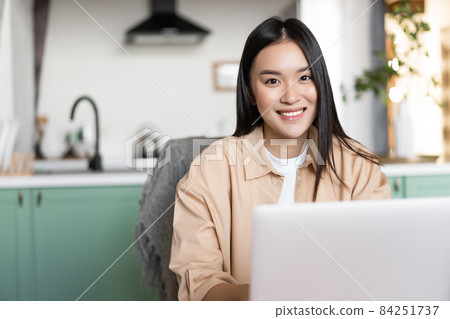 Smiling asian woman working from home with laptop. Happy girl using computer to study or work, freelance and remote education concept Smiling asian woman working from home with laptop. Happy girl using computer to study or work, freelance and remote education concept 84251737