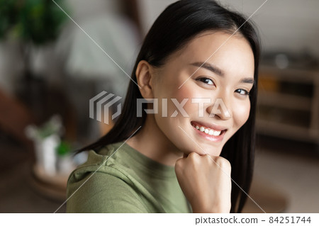 Portrait of young asian woman with clean glowing skin, looking and smiling at camera, sitting at home alone in living room. Lifestyle concept 84251744