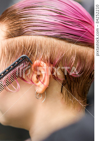 Combing the hair of a young woman during coloring hair in pink color at a hair salon close up. Combing the hair of a young woman during coloring hair in pink color at a hair salon close up. 84252210
