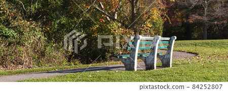 Cement bench with green wood planks looking at the colorful autumn foliage of the woods 84252807