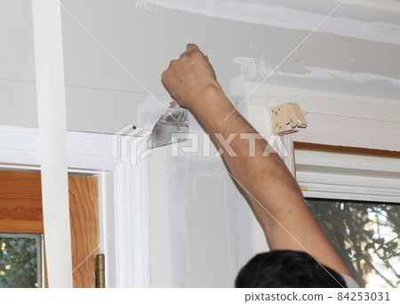 Contractor applying spackle and tape to a wall in a house under constructioin Contractor applying spackle and tape to a wall in a house under constructioin 84253031
