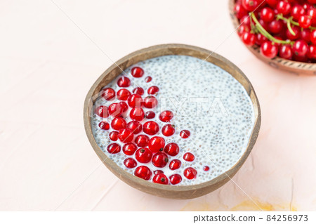 Fresh red currant berries and overnight chia seed pudding in a coconut bowl. Close up, top view, flat lay. Superfood, vegan and raw food concept. Pink background, copy space Fresh red currant berries and overnight chia seed pudding in a coconut bowl. Close up, top view, flat lay. Superfood, vegan and raw food concept. Pink background, copy space 84256973