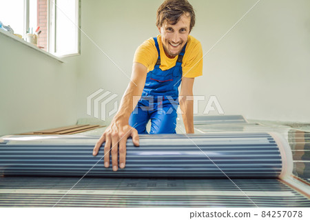 Master installs film warm floor in the room. Floor heating installation Master installs film warm floor in the room. Floor heating installation 84257078