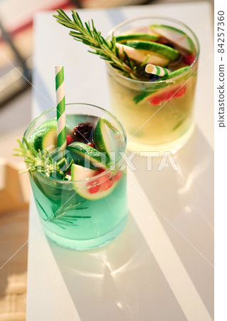 Mojito, fresh alcoholic green cocktail or lemonade with lime,red berries, ice and rosemary in glasses. .Summer vocation concept.top view.Sun and shadows. 84257360